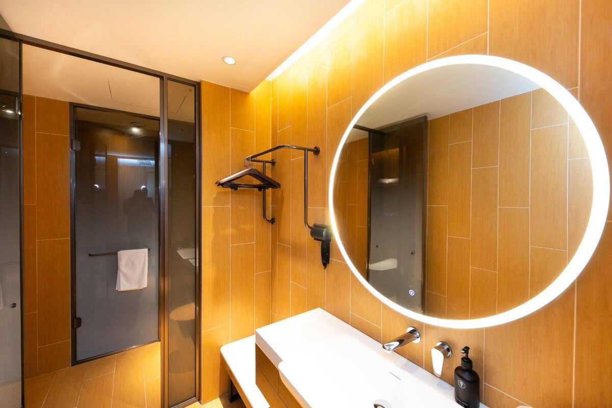 A modern bathroom with a large mirror, wooden wall tiles, a bench, and a towel rack.