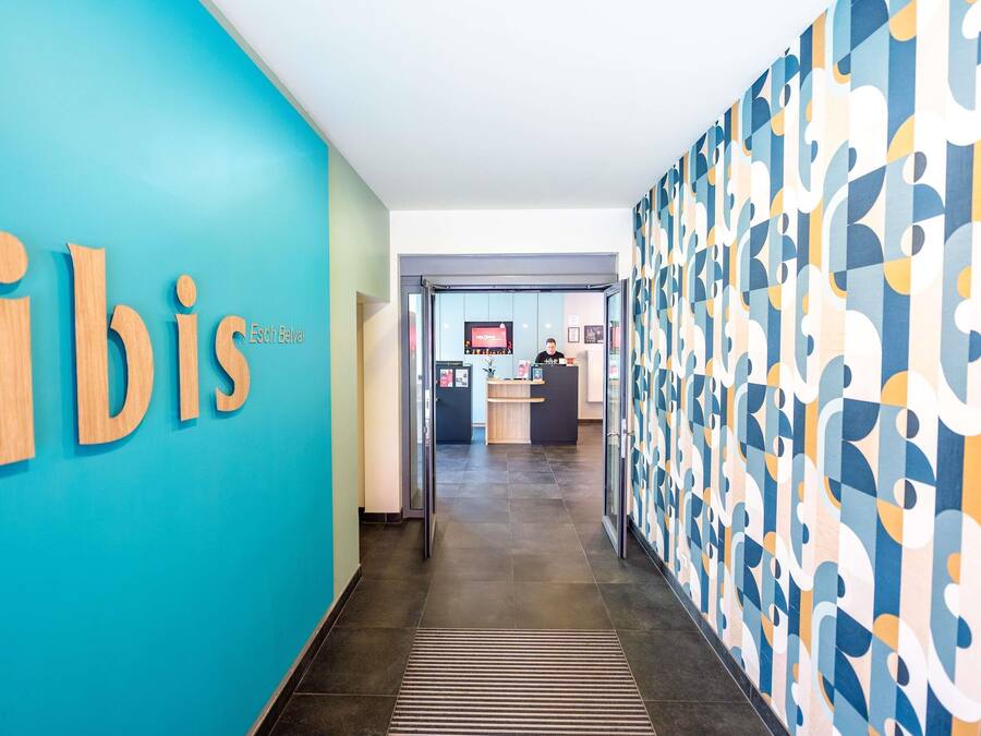 A hallway with a reception desk, a blue wall with the word 'bis' partially visible, and a patterned wall on the right.
