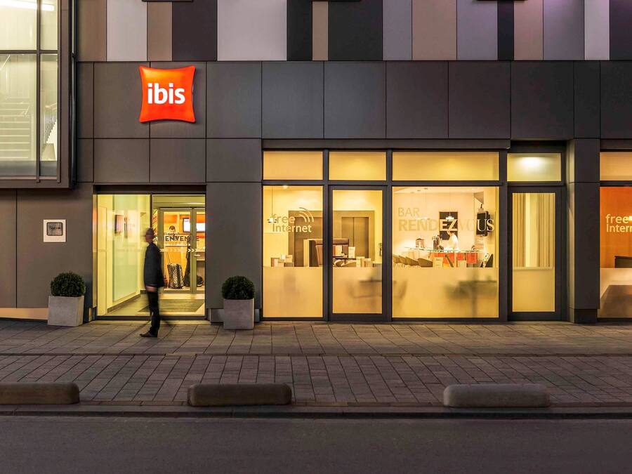 A modern hotel with a prominent 'ibis' sign, a bar/lounge area, and a 'free internet' sign visible through the windows.