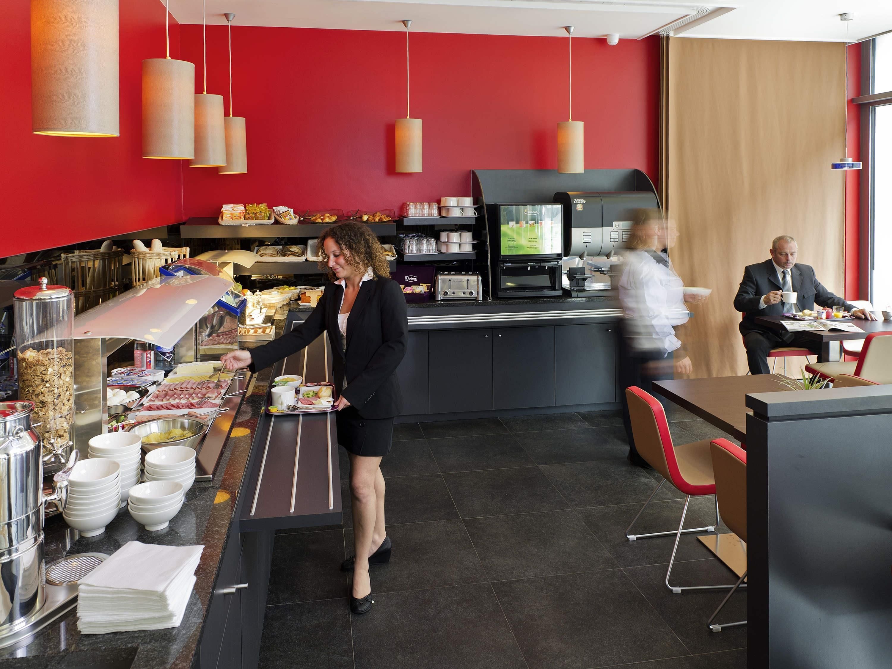 A modern cafe with a red wall, a coffee machine, and a buffet counter.