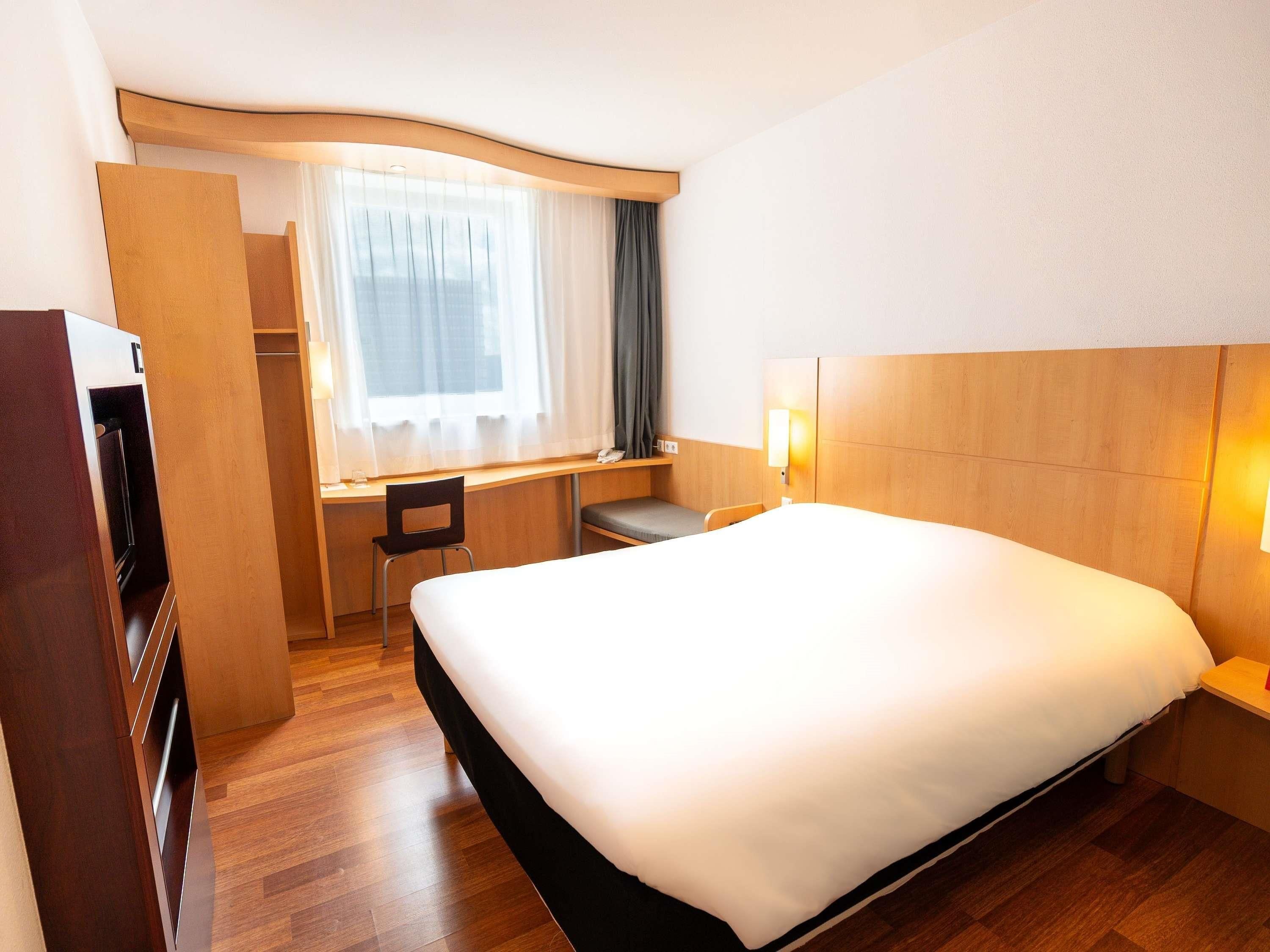 Quarto de hotel com cama, escrivaninha, cadeira e guarda-roupa.