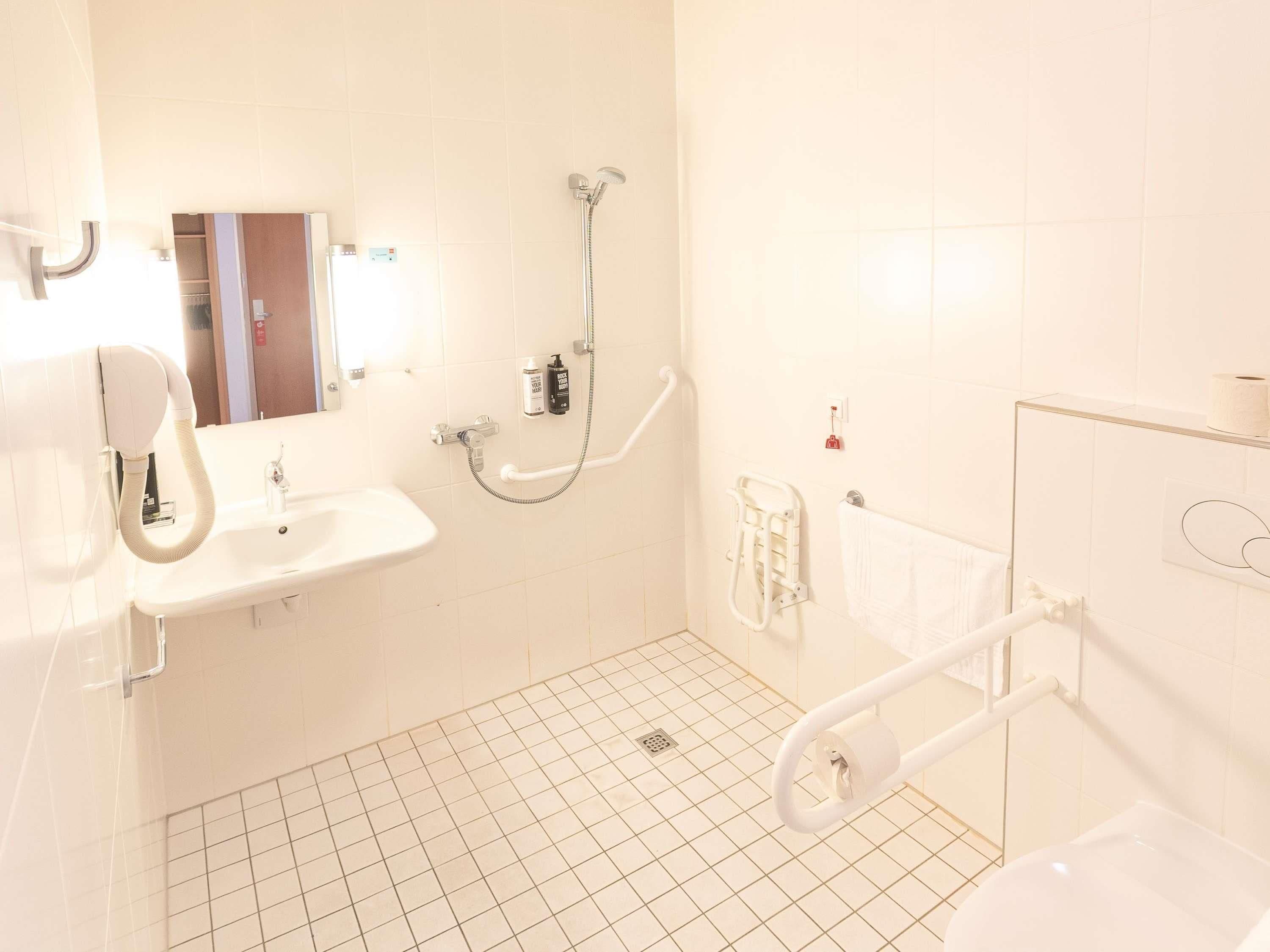 Een badkamer met een wastafel, spiegel, douche en greepstangen.
