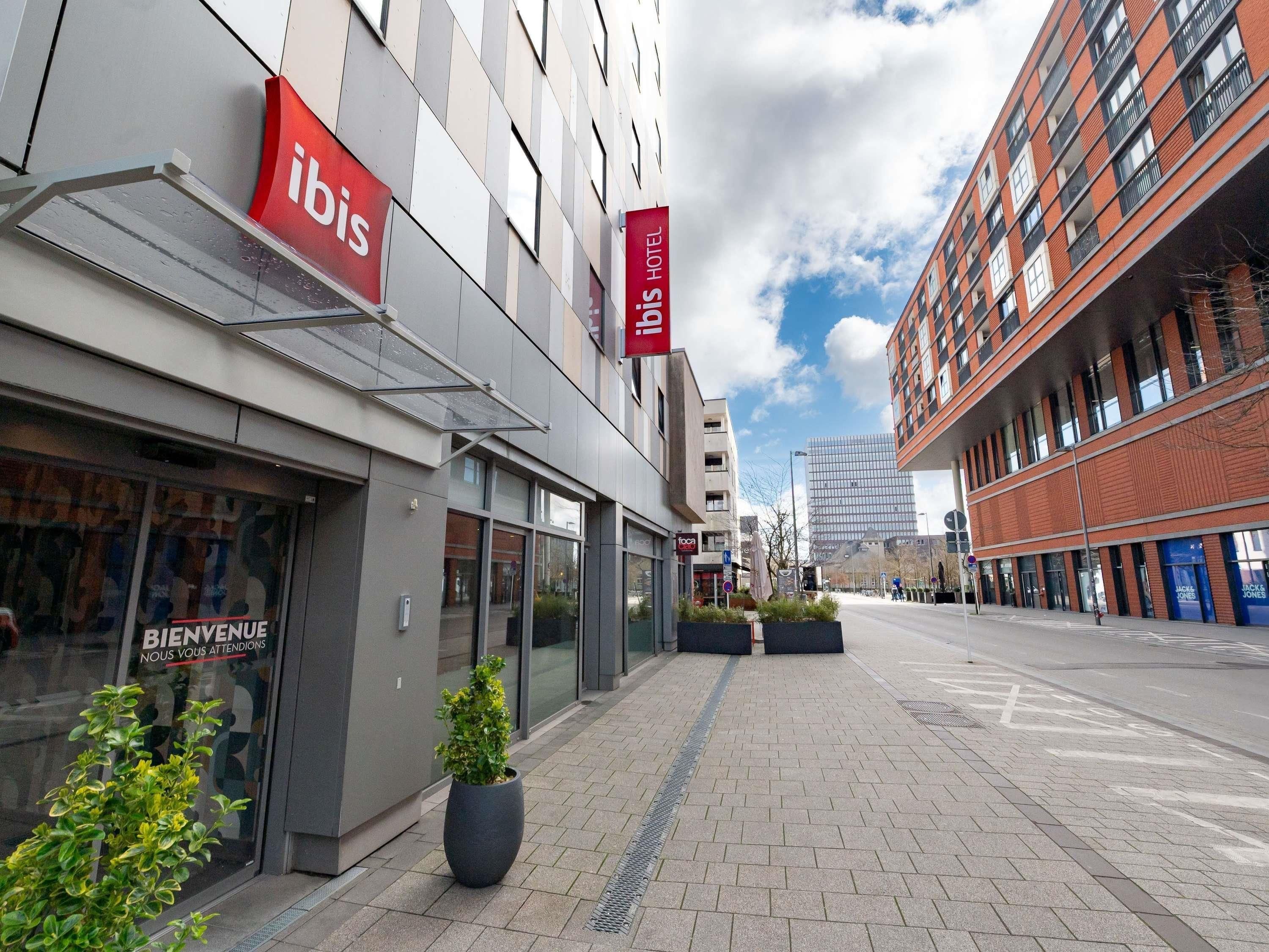Fachada moderna de un hotel con letreros que indican 'ibis' y 'HOTEL'.