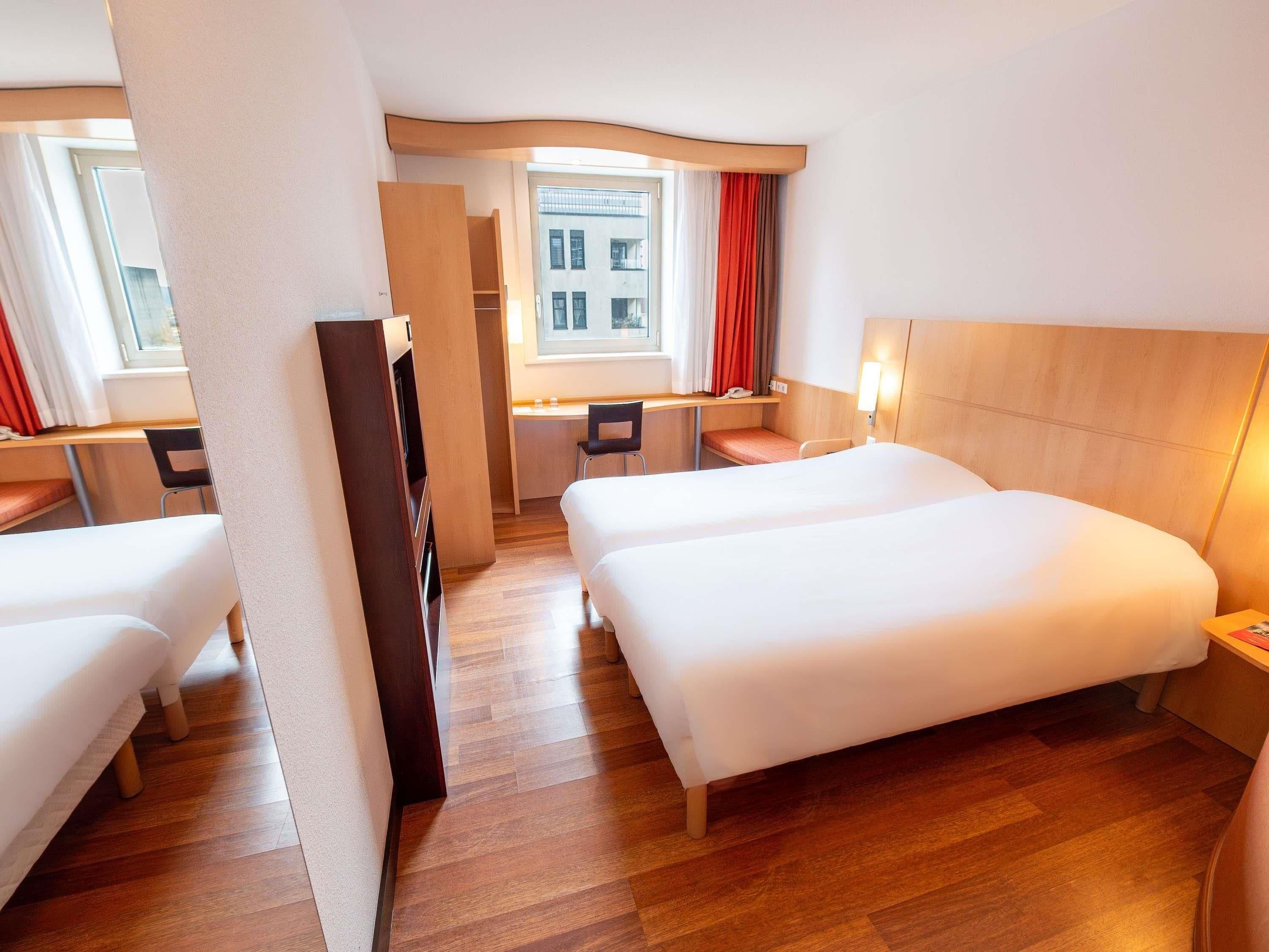 Une chambre d’hôtel avec deux lits, un bureau, une chaise et une fenêtre avec des rideaux.