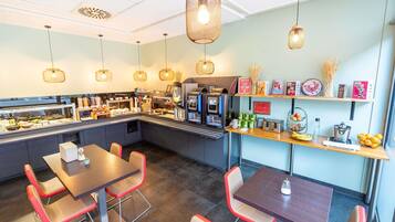 Cafetería con mostrador, zona de mesas y diferentes productos alimenticios a la vista.