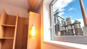 A room with a window overlooking an industrial area, wooden furniture, and a small table with glasses. - ibis Esch Belval (Esch-sur-Alzette)