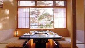 A traditional Japanese-style room with tatami flooring, a low table with cushions, and a large window with a view of trees. - Hyoe Koyokaku (Kobe)