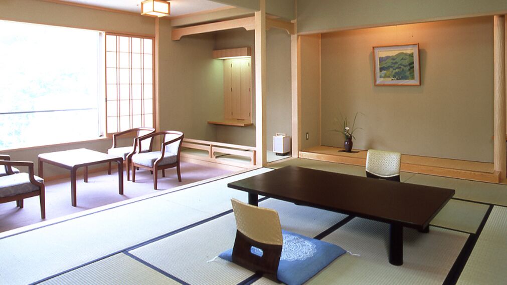 Una habitación tradicional japonesa con suelo de tatami, una mesa baja, sillas y una puerta corredera.