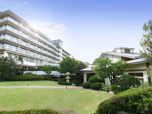 Un hotel de varios pisos con un patio ajardinado, que incluye una fuente y arbustos cuidados.