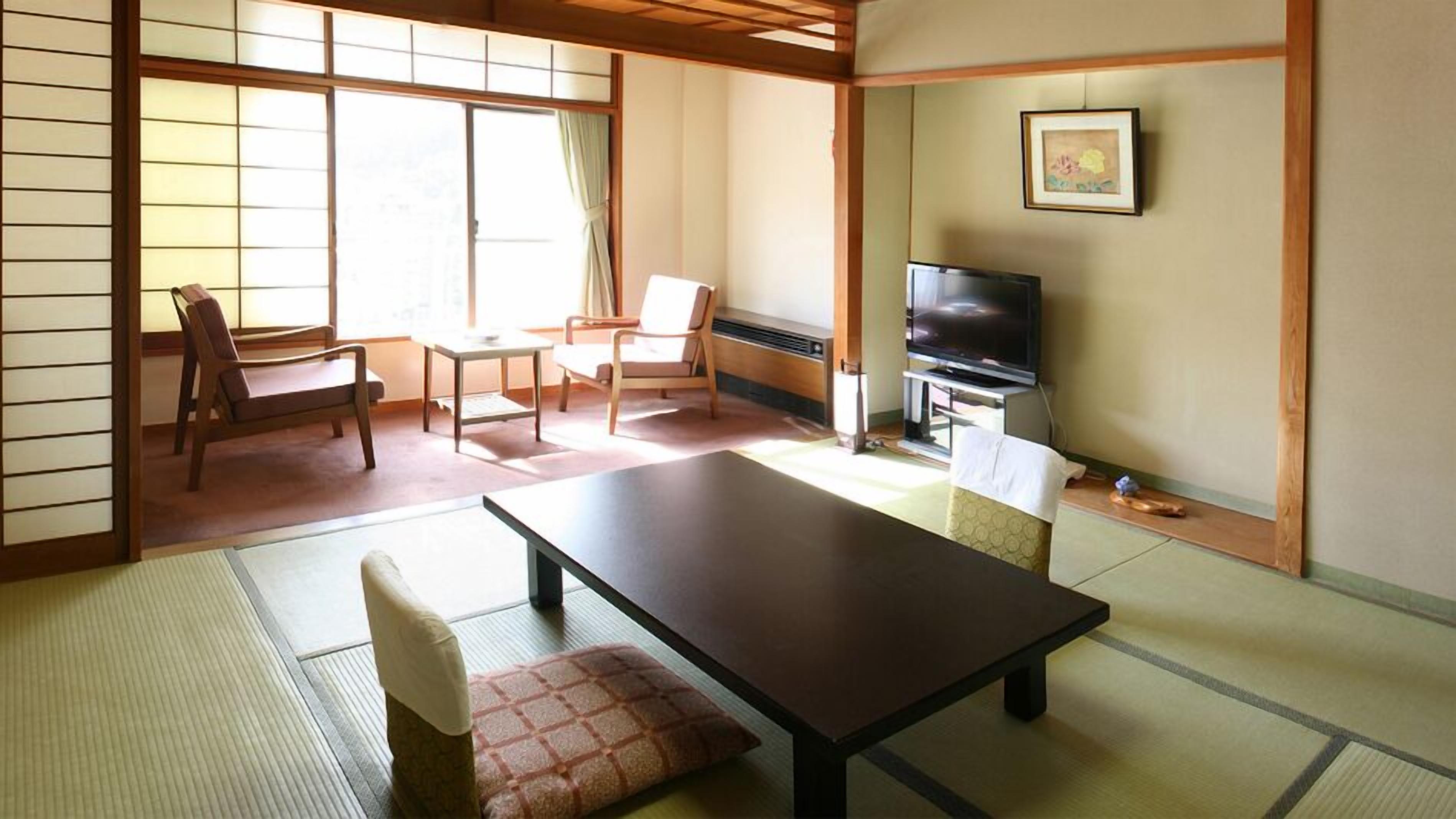 Una habitación japonesa tradicional con suelo de tatami, una mesa baja, sillas, un televisor y una puerta corredera.
