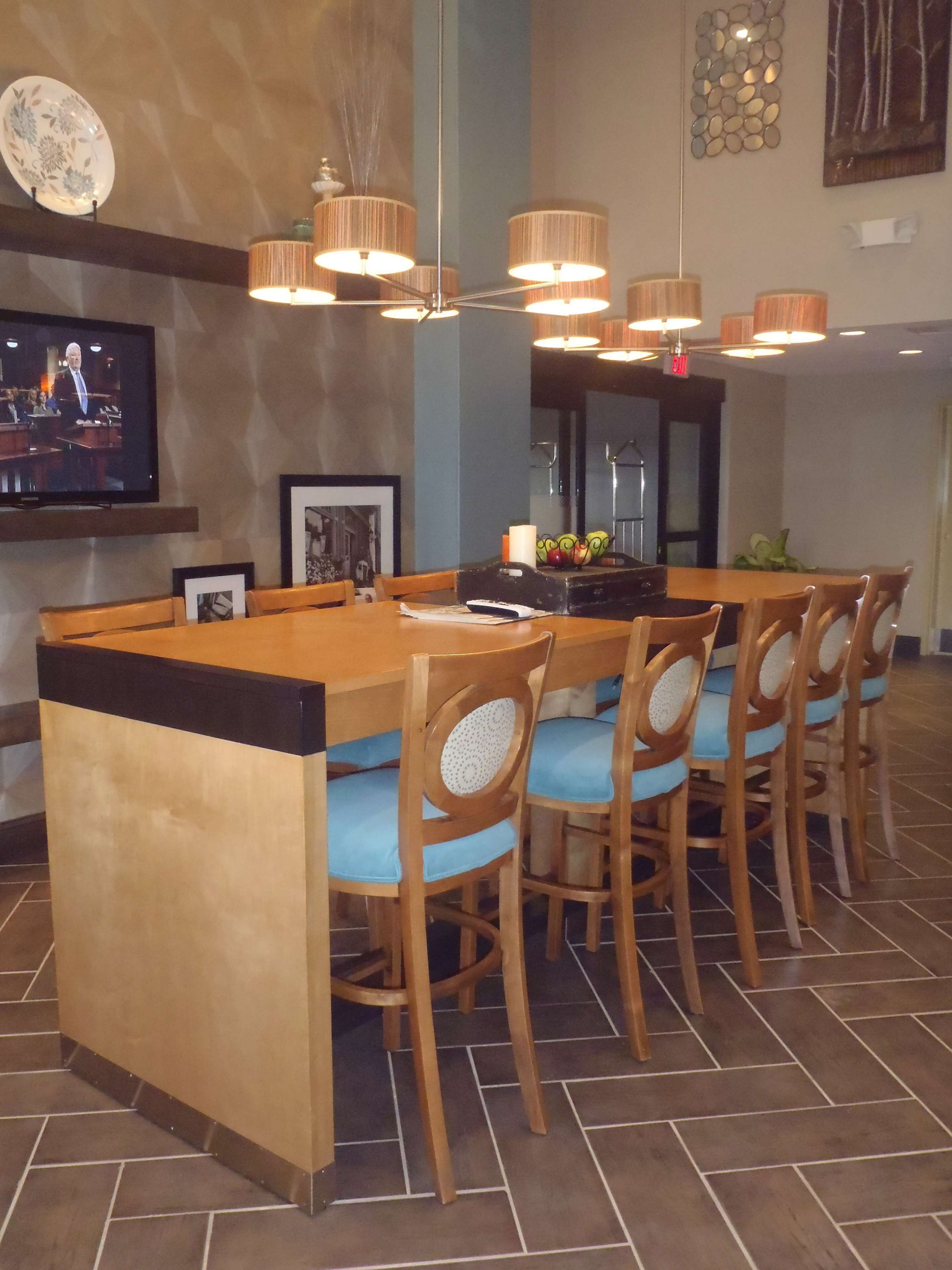 A bar area with a long counter, multiple chairs with blue cushions, and a television screen displaying a news broadcast.