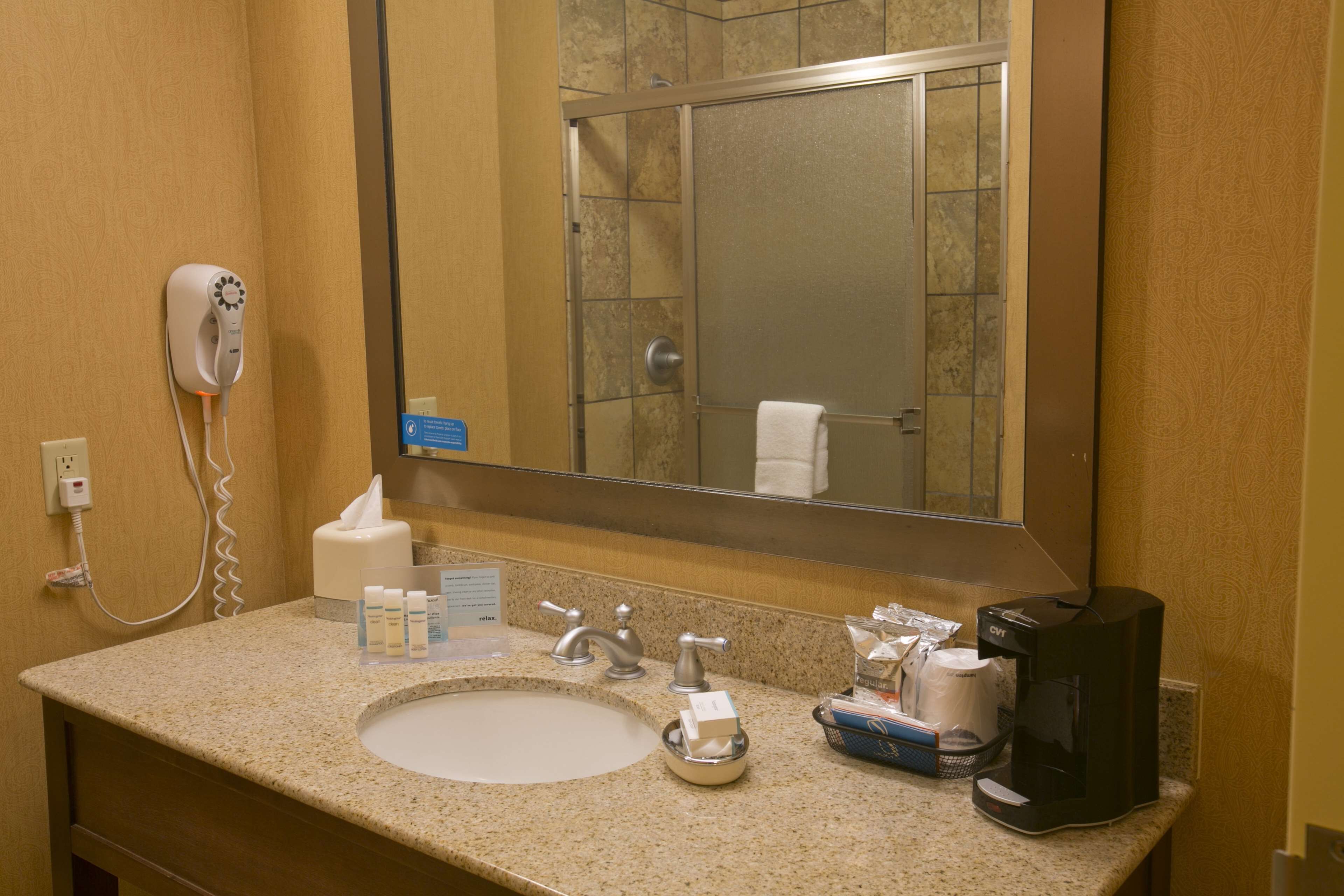 A hotel bathroom with a sink, mirror, towel rack, and a hairdryer on the wall.