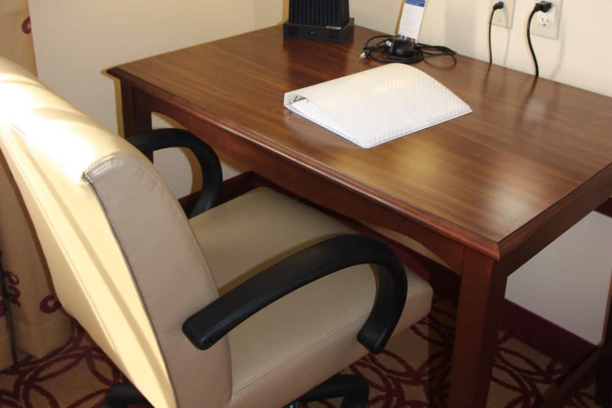 A hotel room with a wooden desk, a white chair, a lamp, and a mirror.
