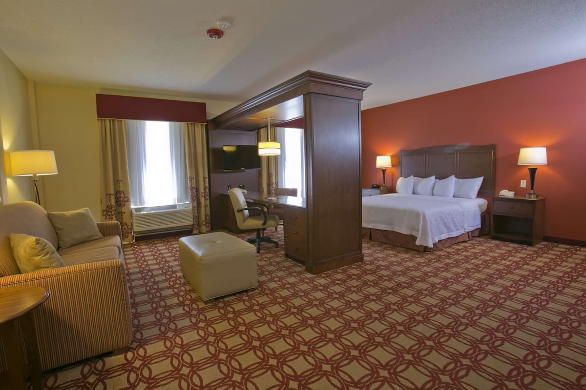 A hotel room with a bed, a sofa, a desk, a chair, and a lamp.