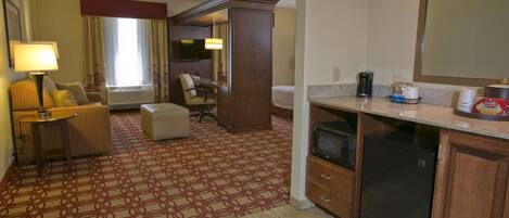 Habitación de hotel con alfombra estampada, sofá, escritorio, televisor, refrigerador y microondas.