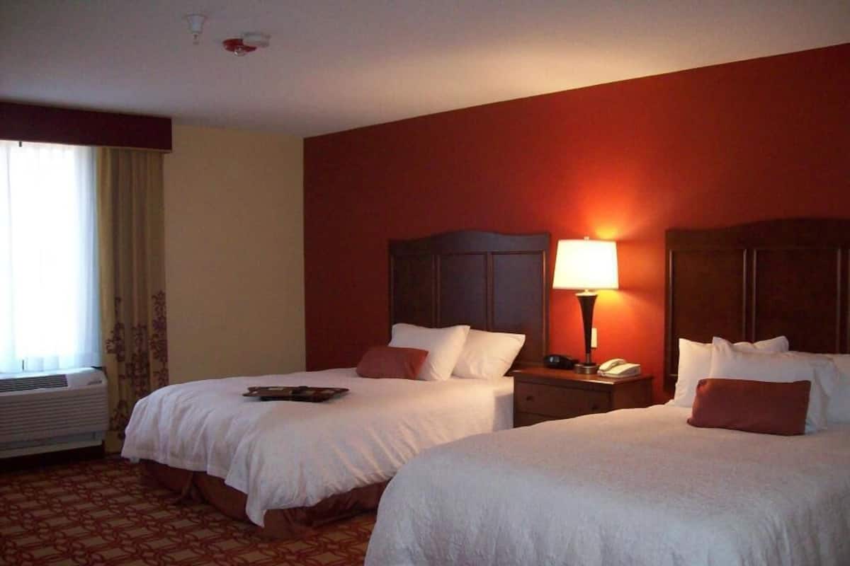 A hotel room with two beds, a bedside lamp, a telephone, and a window with curtains.