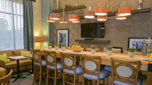 A dining area with a long wooden table, six chairs, and a TV mounted on the wall. - Hampton Inn & Suites Wiggins (Wiggins)