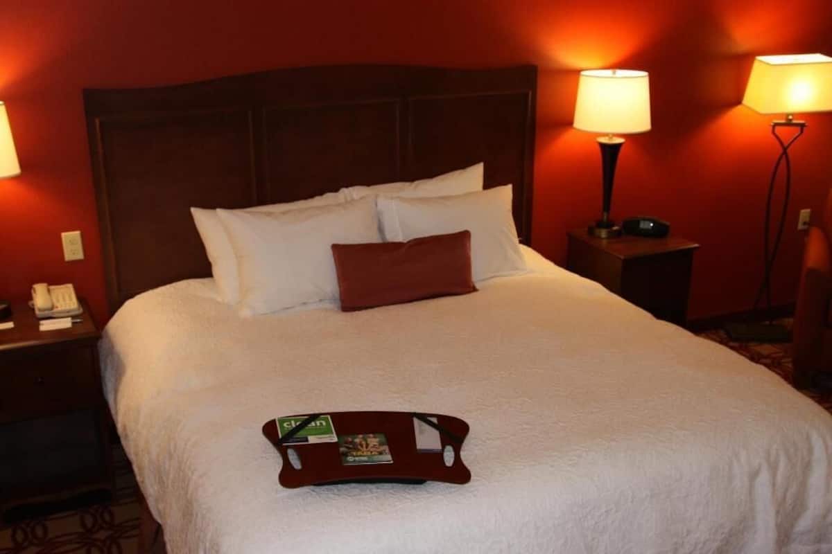 A hotel room with a large bed, two bedside tables, and a tray with a magazine on the bed.
