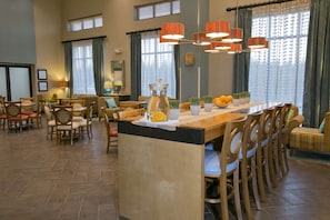 A spacious dining area with a long wooden table, multiple chairs, and a central island with a pitcher and oranges.