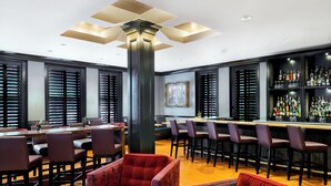 A bar area with a long counter, multiple bar stools, and a high ceiling with recessed lighting. - Inn at Carnall Hall (Fayetteville)