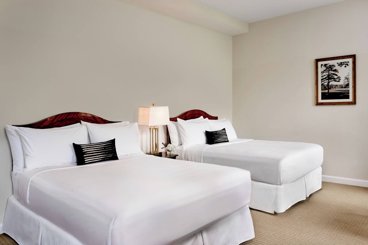 A hotel room with two beds, a nightstand with a lamp, and a framed picture on the wall.