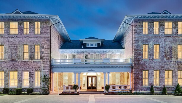 A large, symmetrical building with a central entrance, two-story brick facade, and a balcony with white railings. - Inn at Carnall Hall (Fayetteville)