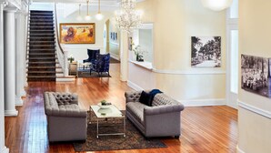 A spacious living area with a grand staircase, a chandelier, and a fireplace. - Inn at Carnall Hall (Fayetteville)