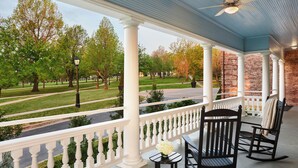 A covered porch with white columns, a brick wall, and a view of a park. - Inn at Carnall Hall (Fayetteville)