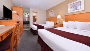 Habitación de hotel con dos camas, un escritorio con televisor, un espejo y una lámpara.