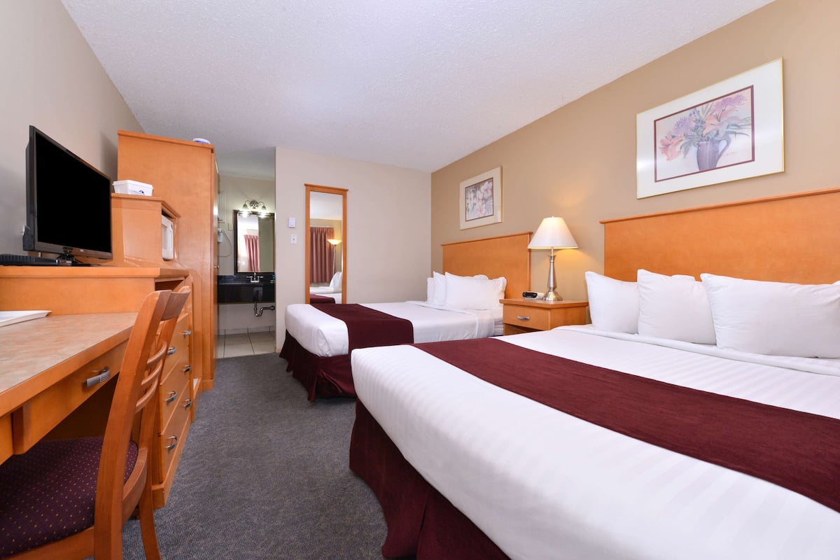 A hotel room with two beds, a desk with a television, a mirror, and a lamp.