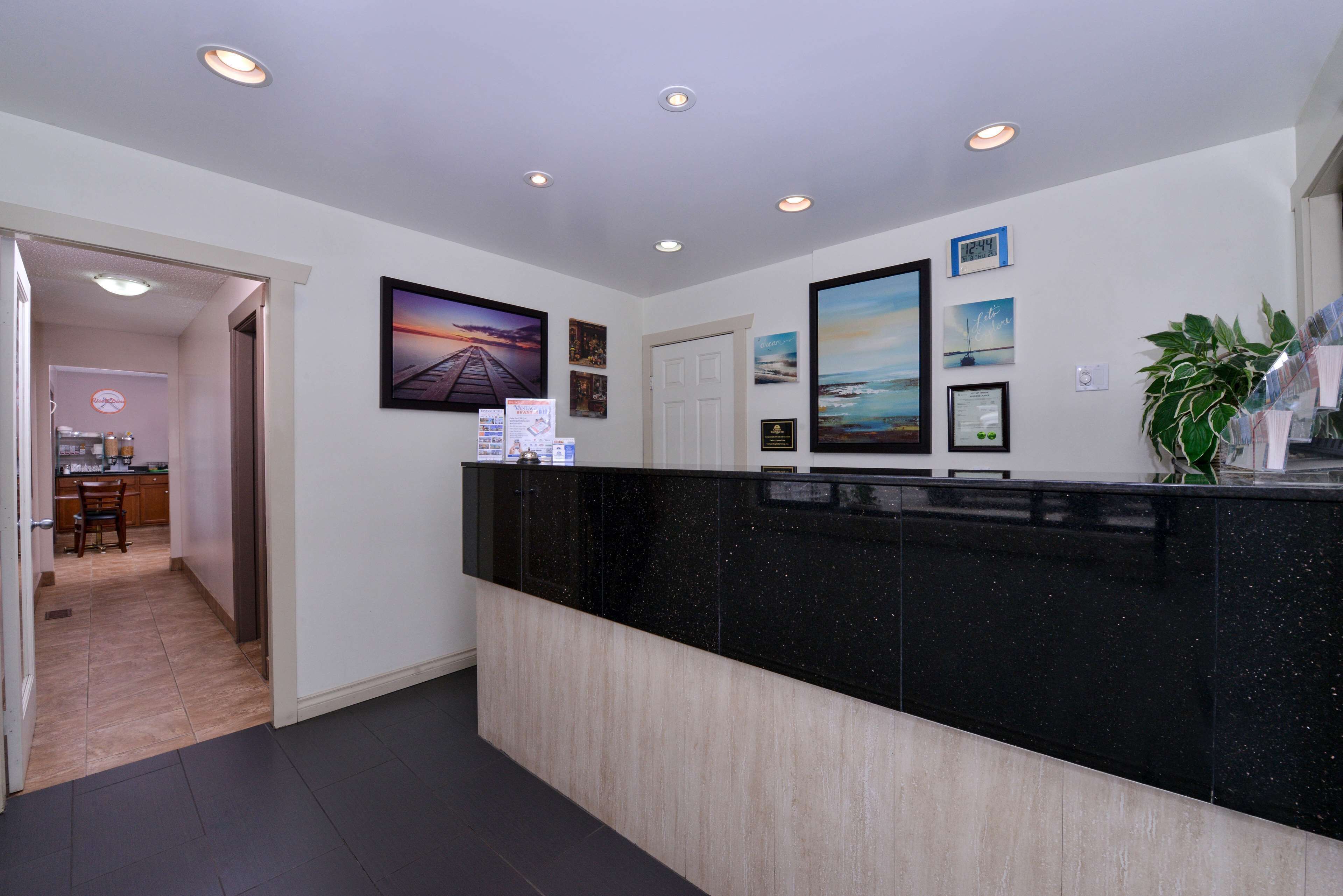A reception area with a black marble counter, framed pictures on the wall, and a door leading to a kitchen.