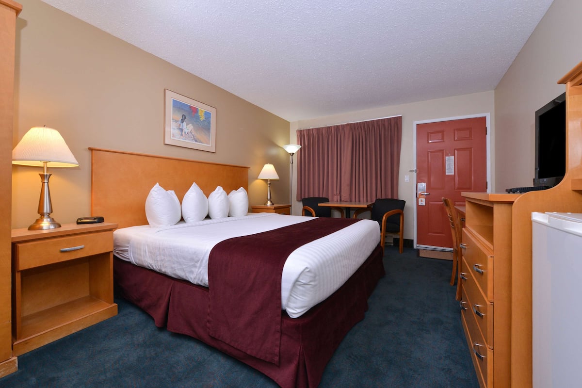 A hotel room with a large bed, two bedside lamps, a desk with a chair, a television, and a door.