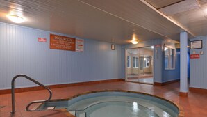 Una piscina interior con suelo de baldosas, barandilla de metal y señalización con las normas de la piscina y prohibición de bebidas.