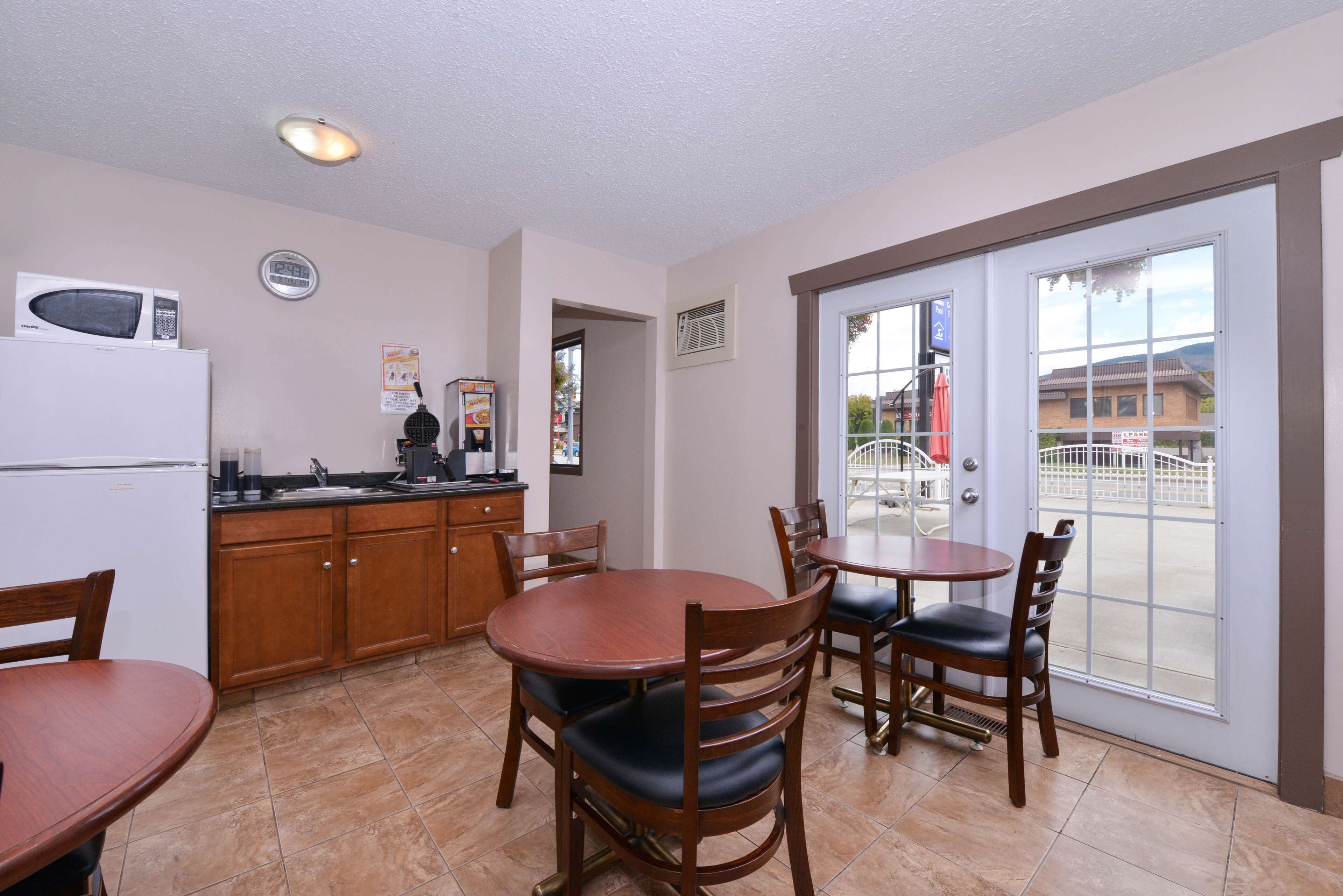A kitchen with a microwave, refrigerator, and a dining area with wooden chairs and a table.