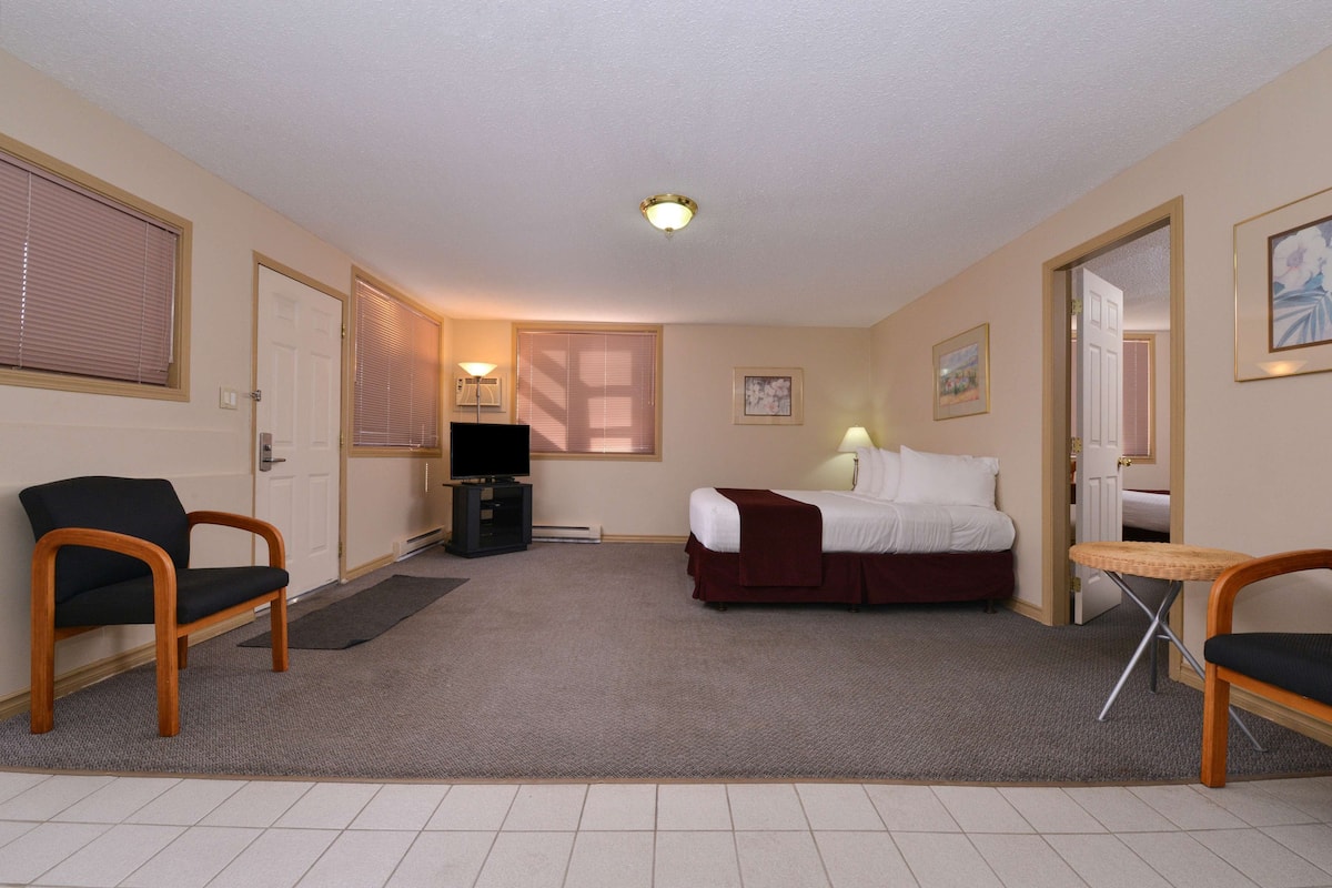 A hotel room with a bed, two chairs, a TV, and a small table.