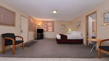 A hotel room with a bed, two chairs, a TV, and a small table.