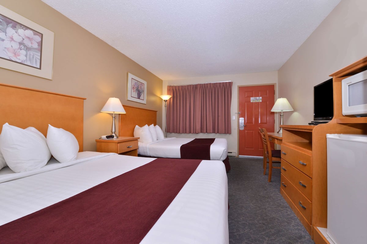 A hotel room with two beds, a desk, a chair, a television, and a dresser.
