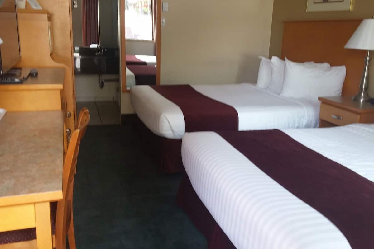 A hotel room with two beds, a desk, a chair, a lamp, and a window.