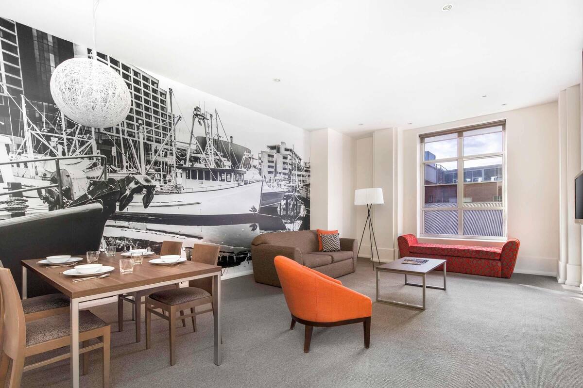 Habitación de hotel con comedor, sofá, lámpara y un amplio ventanal.