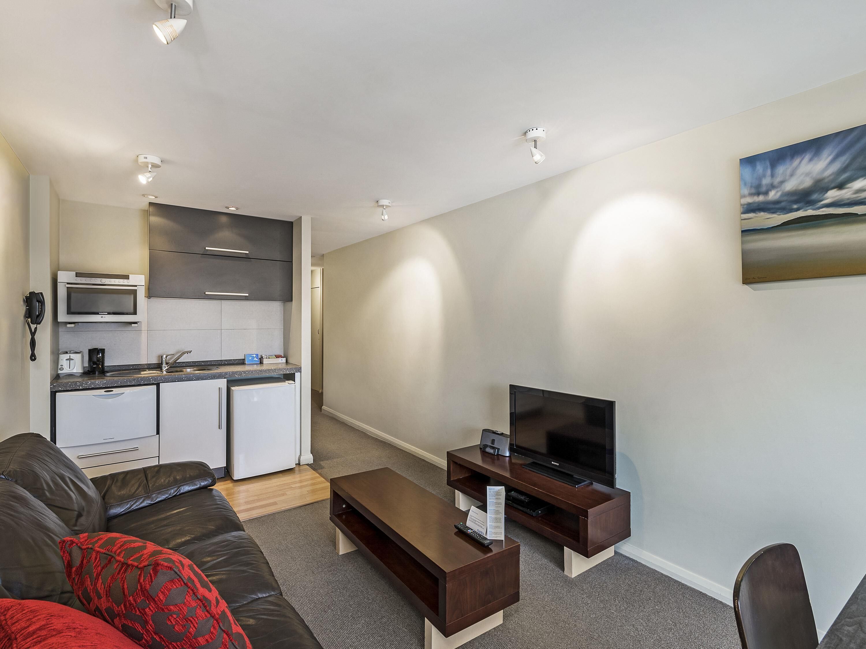 A compact living space with a kitchenette, a flat-screen TV, a sofa, and a coffee table.
