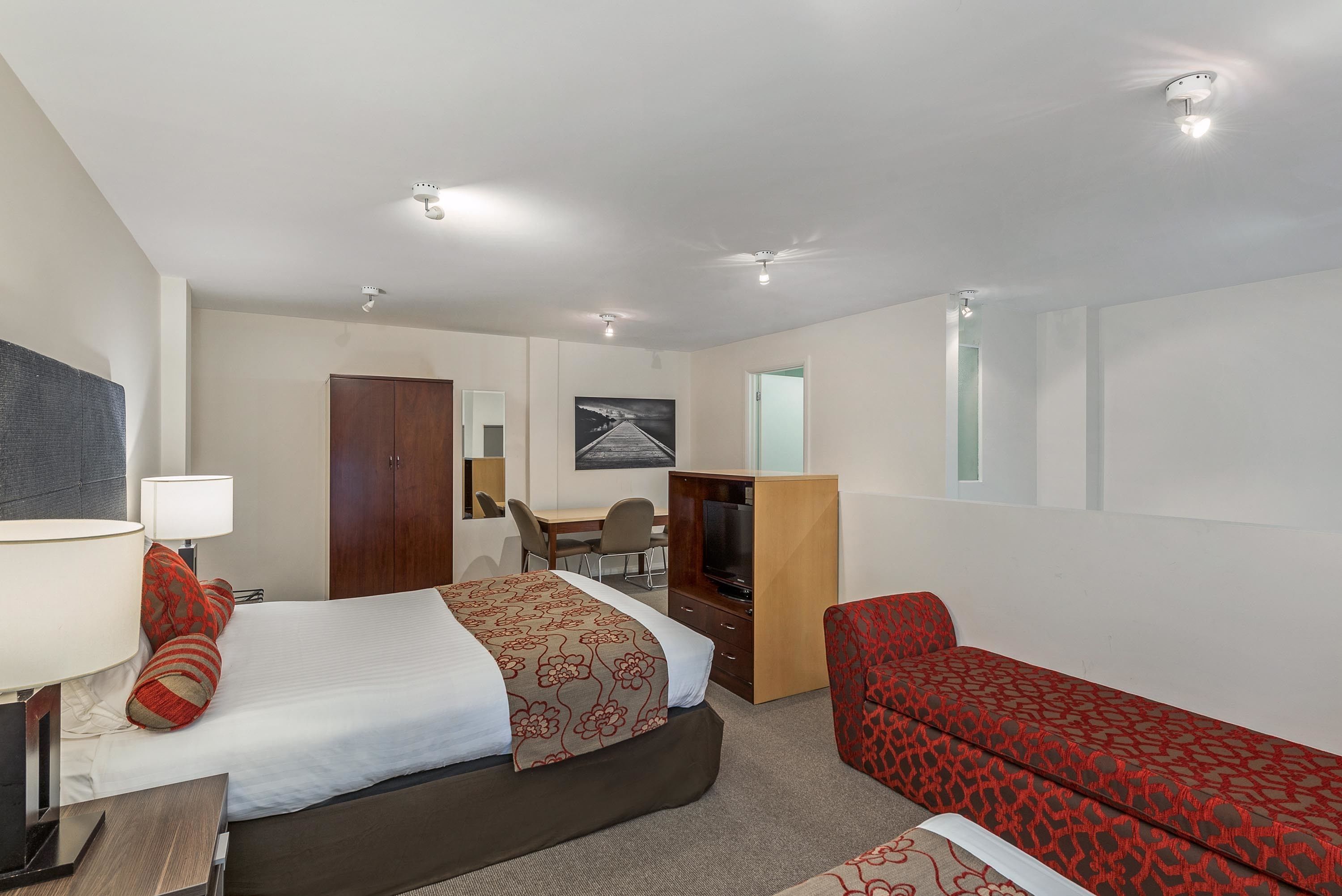 A hotel room with a bed, a desk, a television, and a red sofa.