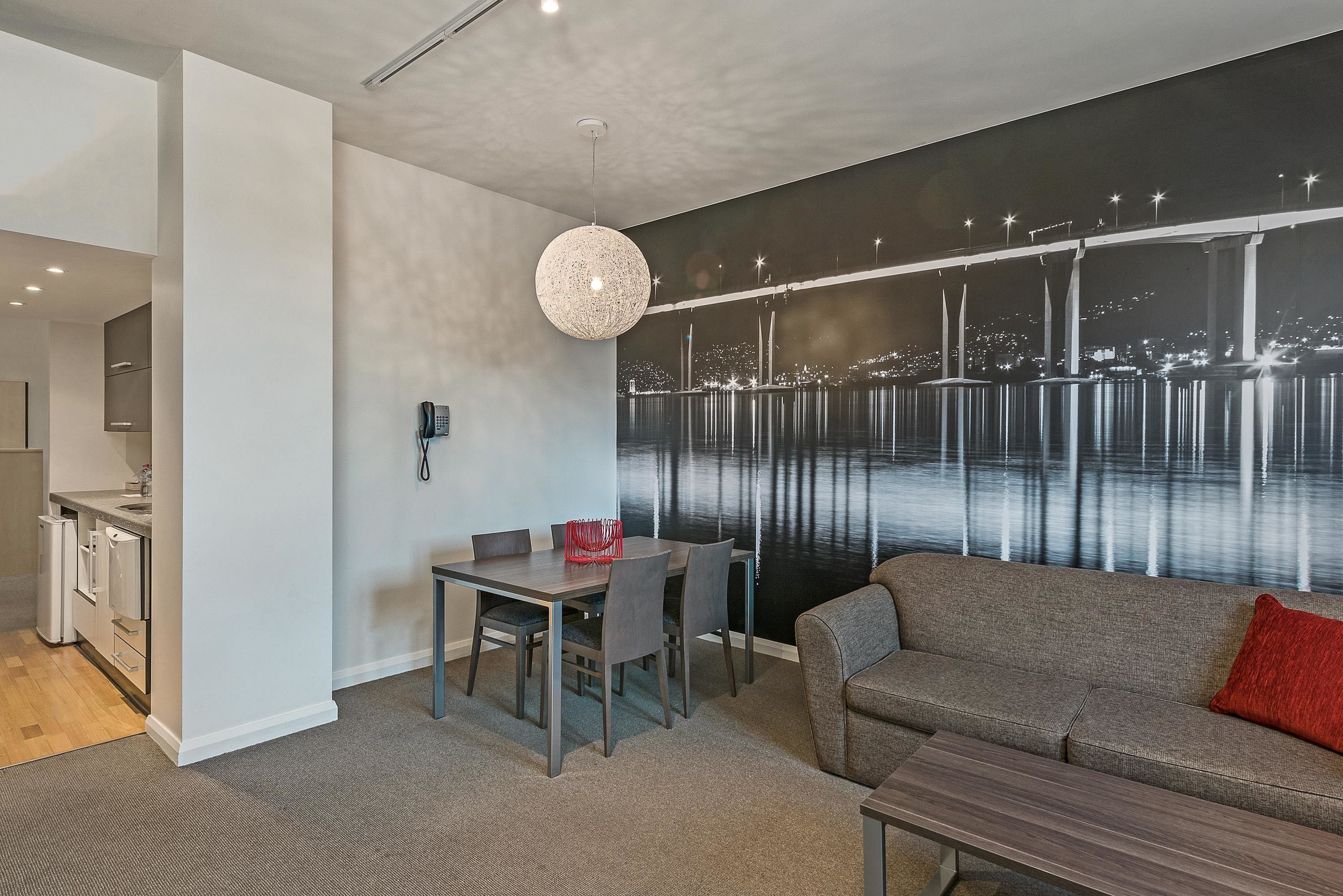 A modern living room with a sofa, a dining table with chairs, and a kitchen area in the background.