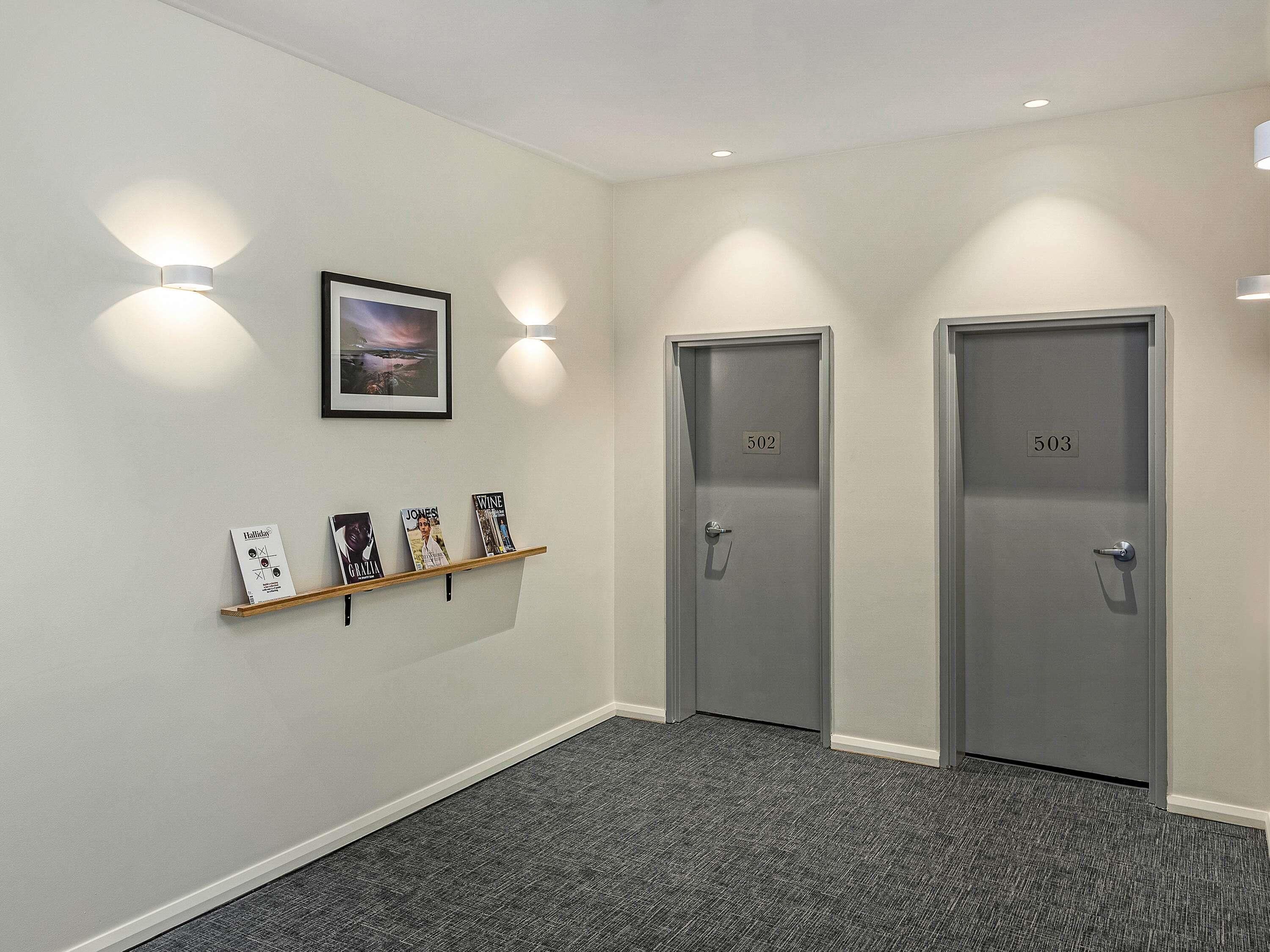 A hallway with two doors labeled 502 and 503, a framed picture on the wall, and a shelf with books.