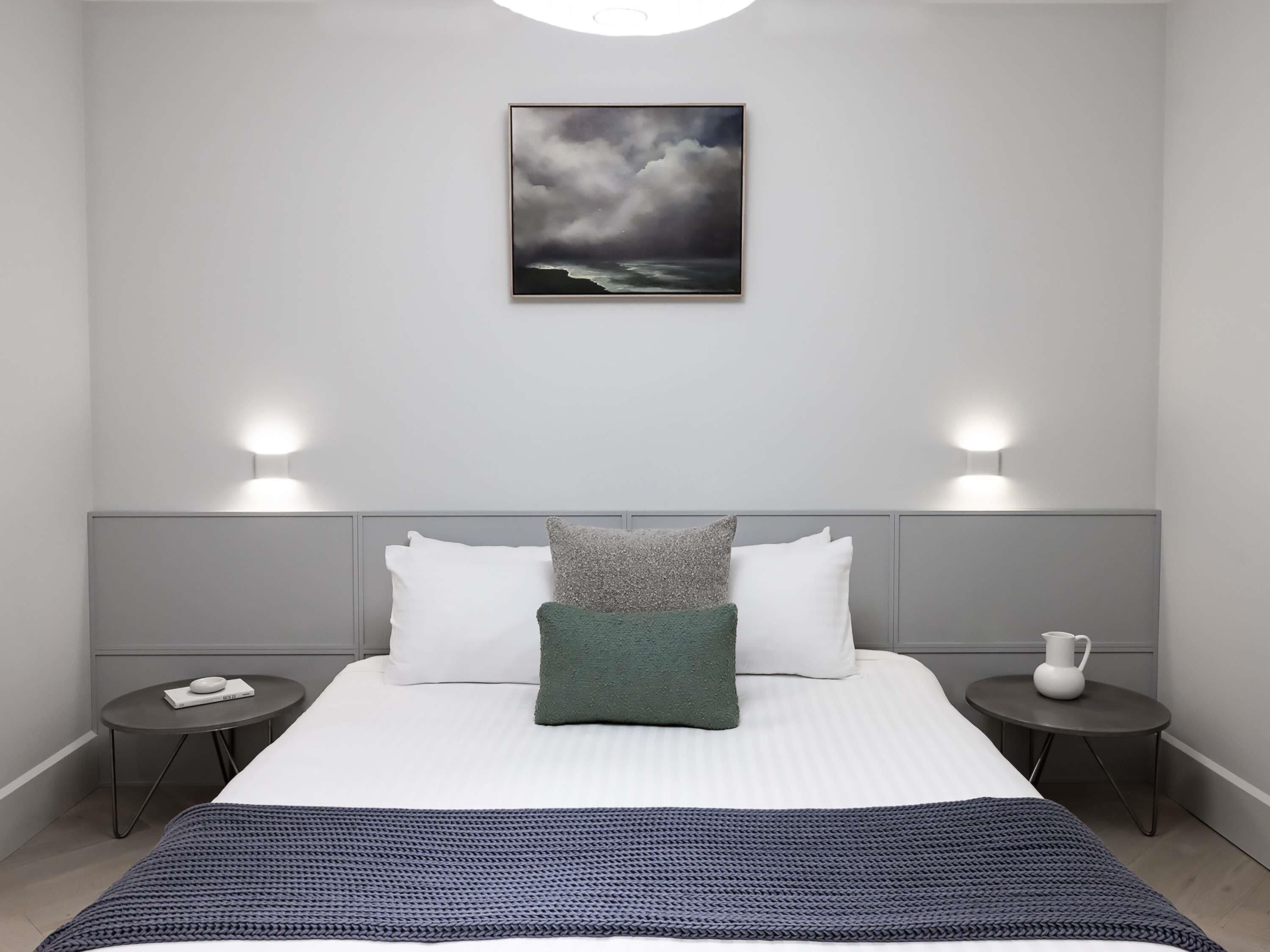 Un dormitorio moderno con una cama, dos mesitas de noche, una lámpara de noche y un cuadro en la pared.