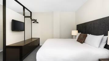 A hotel room with a bed, a TV mounted on the wall, a bedside table, and a lamp.