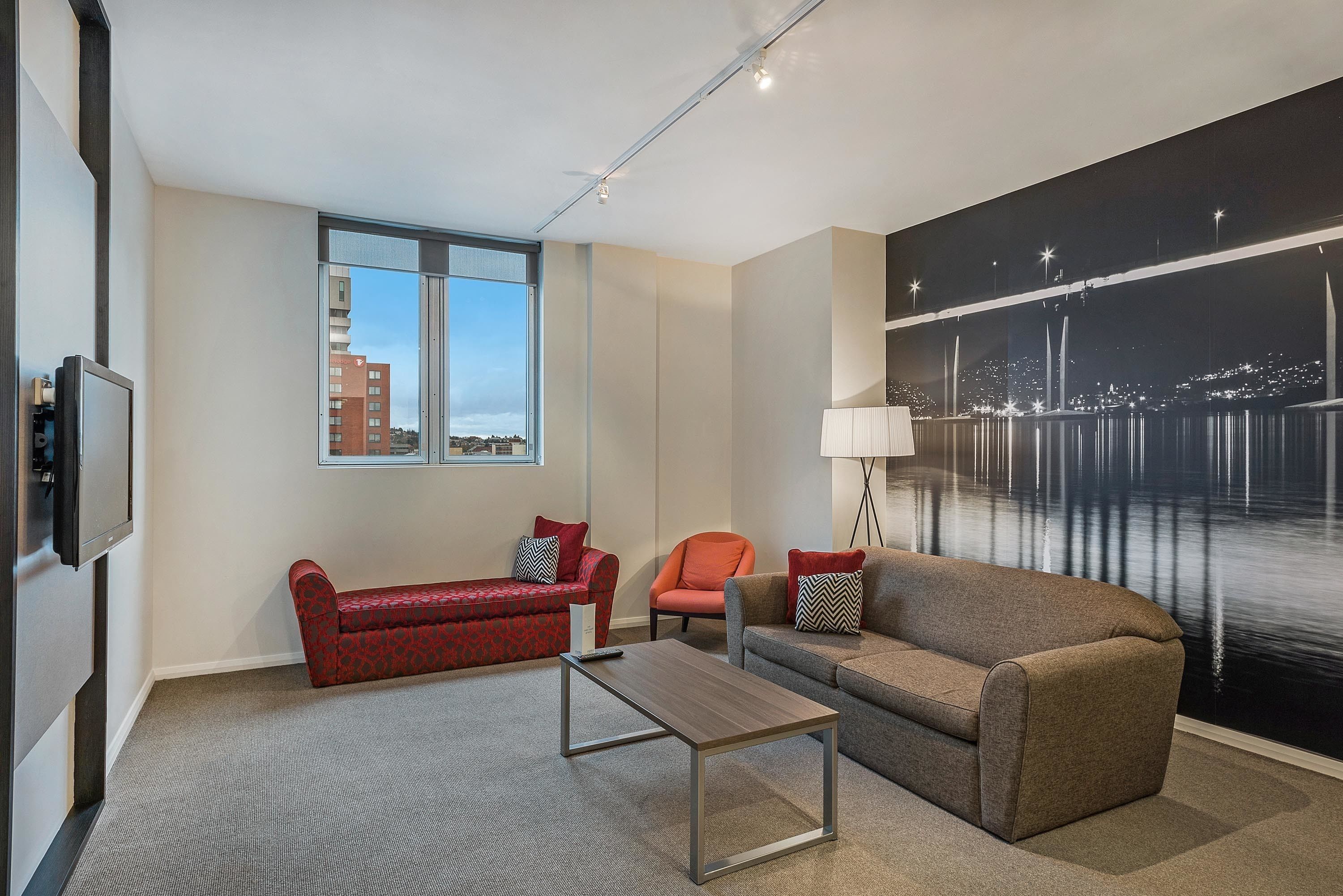 A modern living room with a large window, a flat-screen TV, a coffee table, and two sofas.