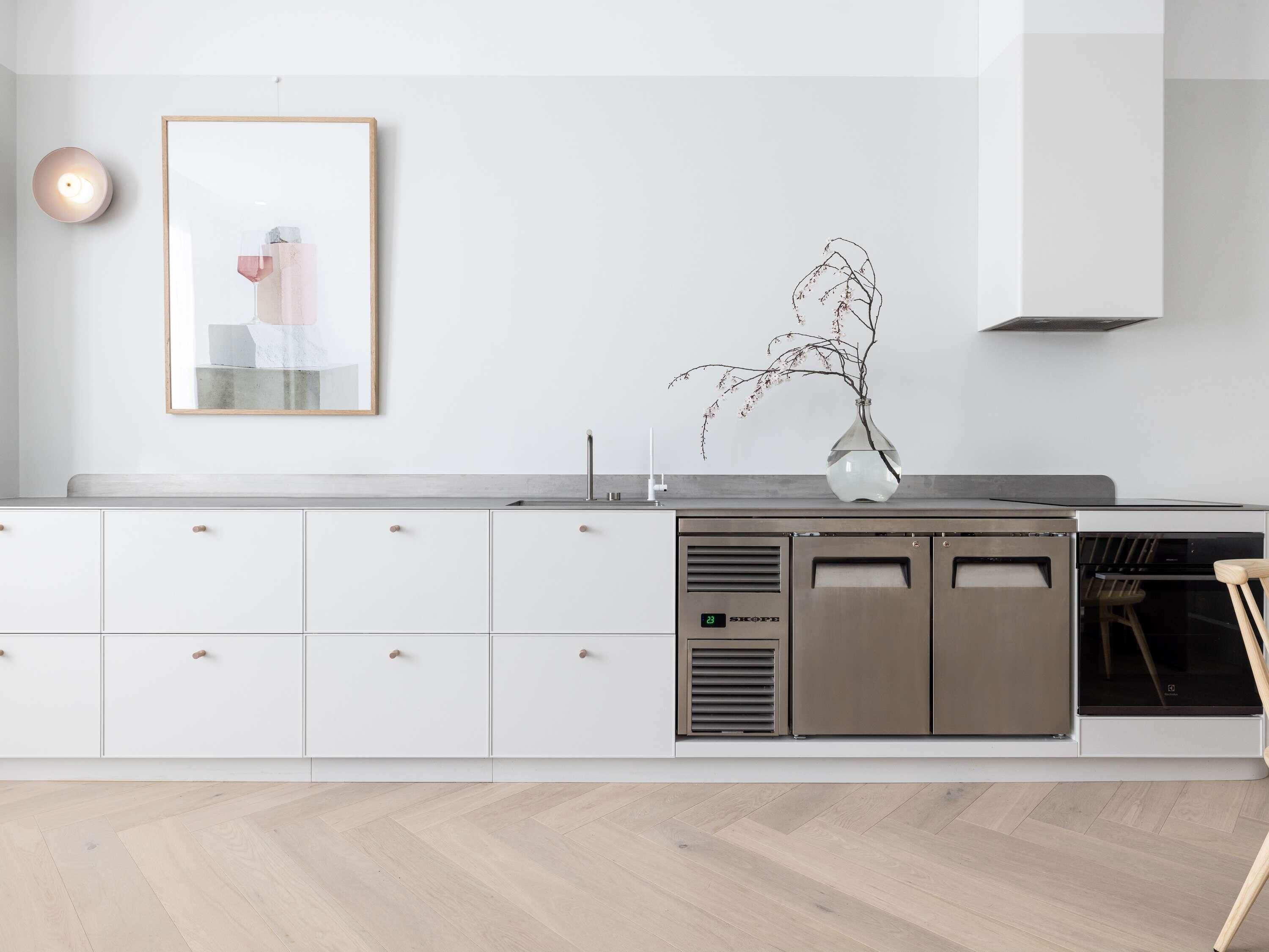 Una cucina moderna con mobili bianchi, una cappa aspirante in acciaio inossidabile e un vaso con rami sul piano di lavoro.
