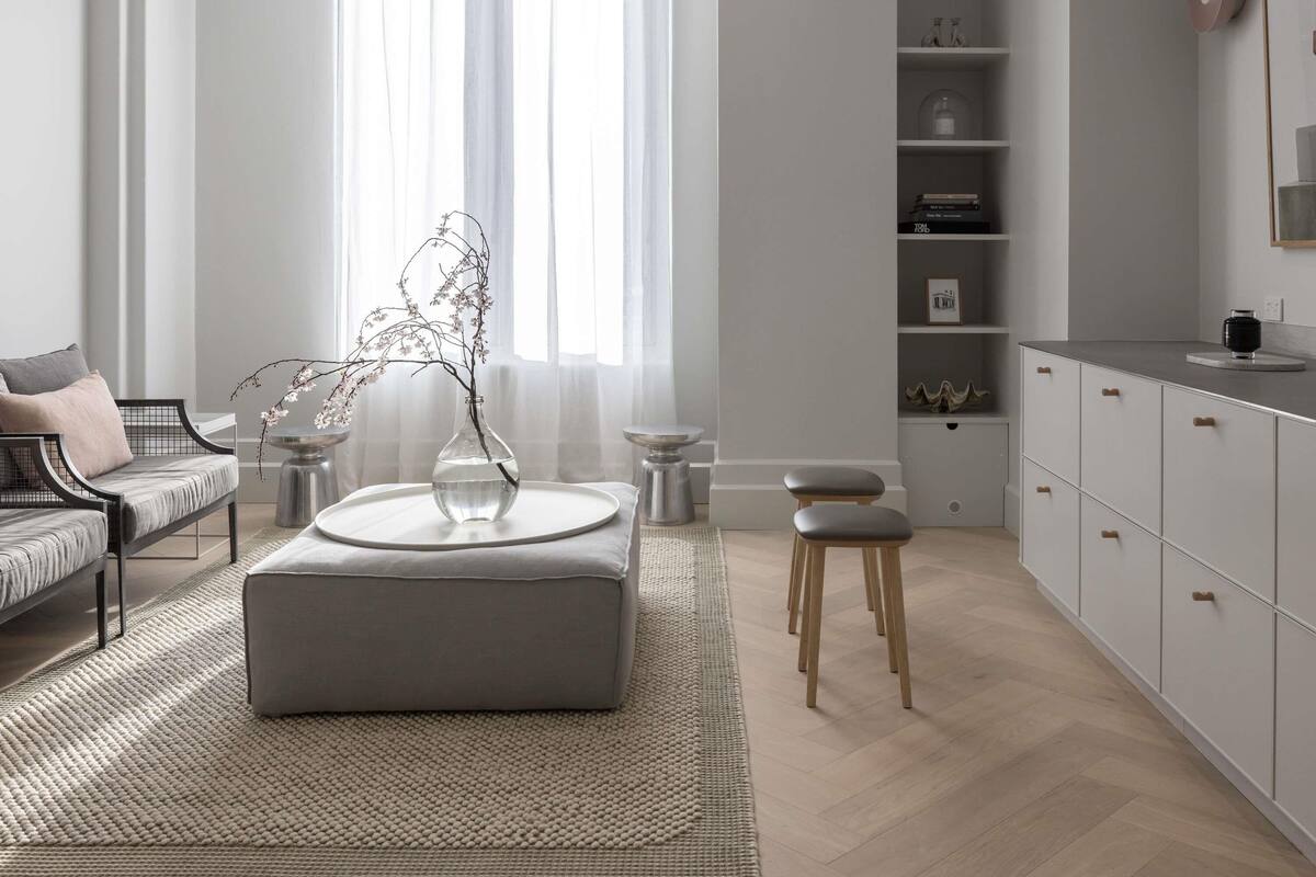 Una sala de estar moderna con un sofá, un reposapiés y un jarrón con ramas.