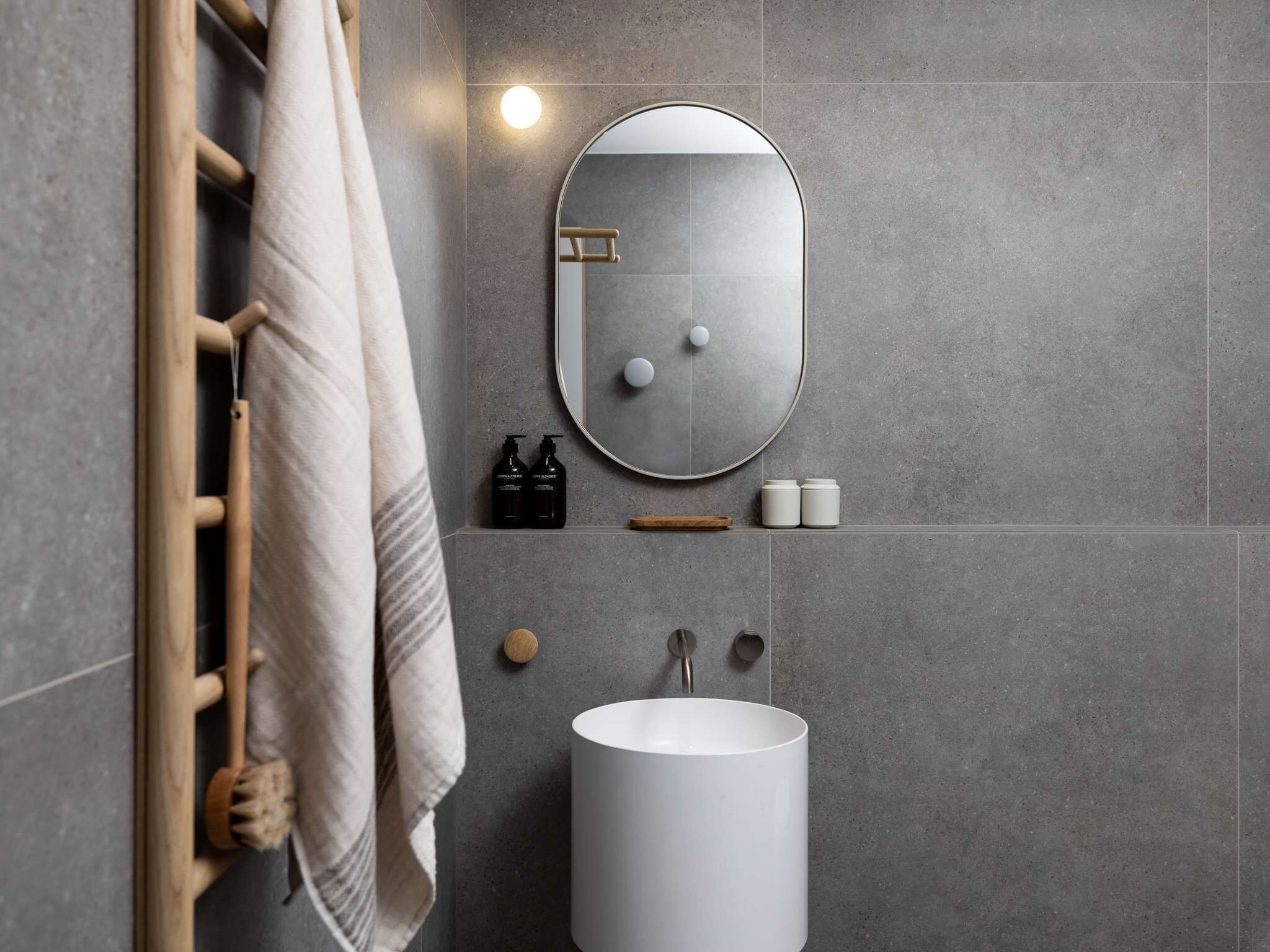 Une salle de bain avec un lavabo blanc, un miroir rond et un porte-serviettes.