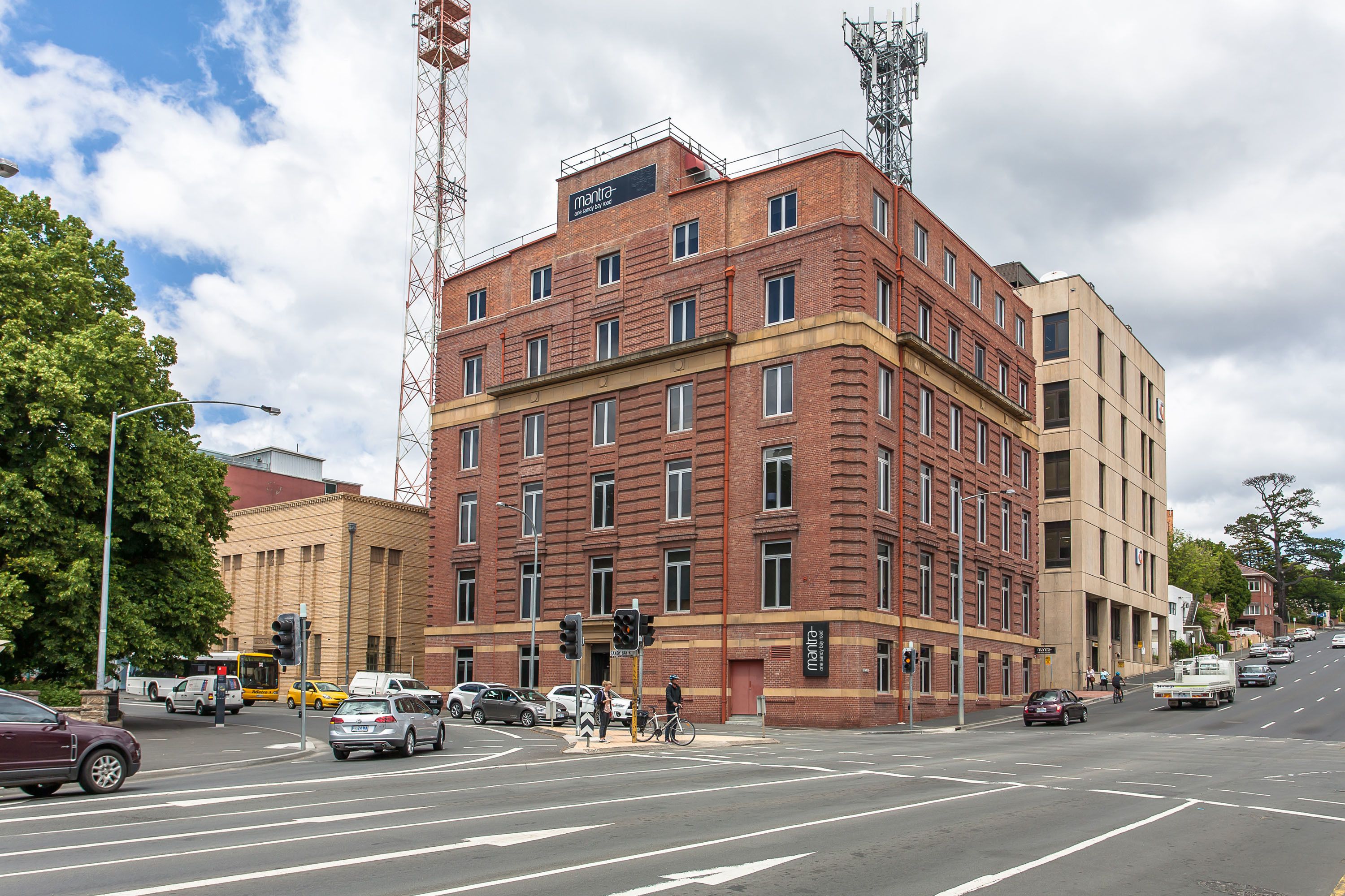 A multi-story building with a prominent red brick facade, a sign reading "Mantra," and a corner location with a street intersection.